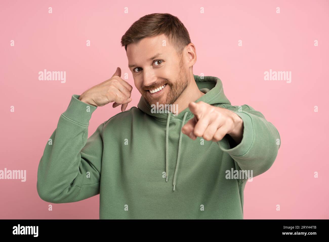 Homme barbu heureux pointant l'index à la caméra, montrant le geste de téléphone appelez-moi sur fond rose. Banque D'Images