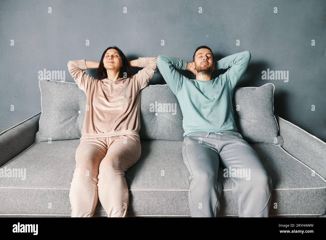 Couple se détendant sur un canapé à la maison s'étirant avec les mains derrière la tête. Banque D'Images