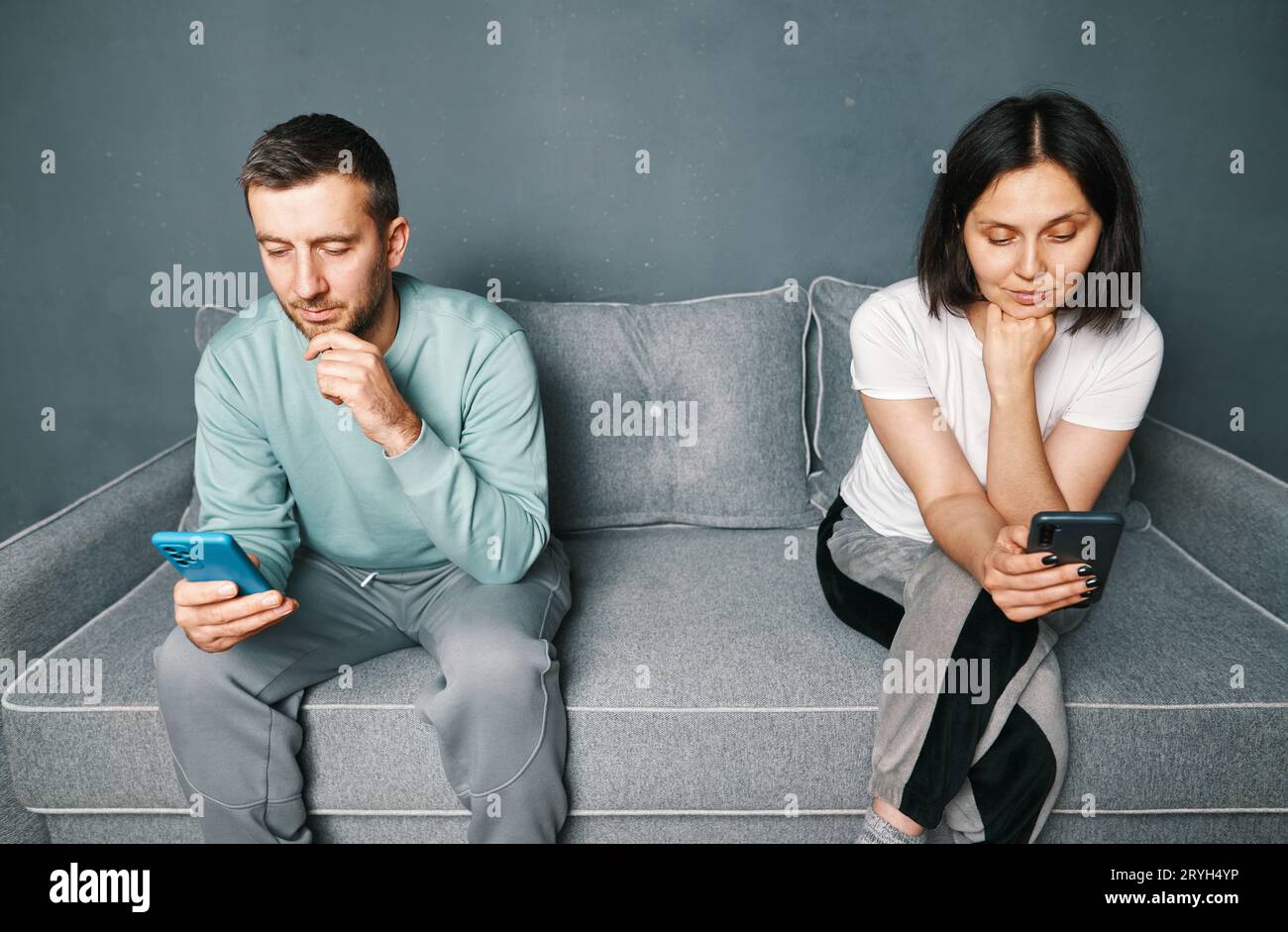 Jeune couple ennuyé assis sur le canapé et regardant leurs téléphones intelligents Banque D'Images