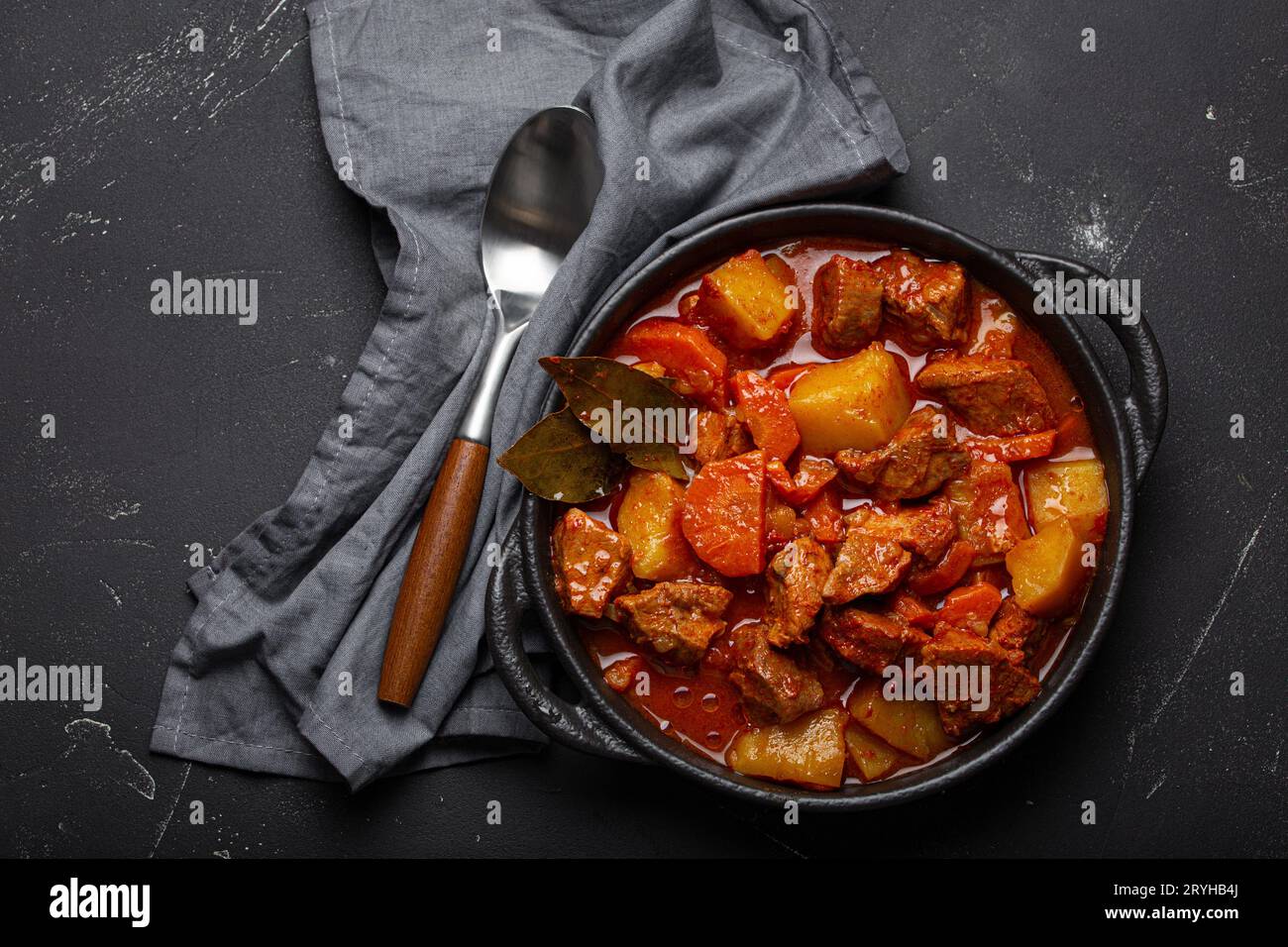 Ragoût de viande de bœuf avec pommes de terre, carottes et sauce délicieuse dans une casserole noire avec feuilles de Laurier et cuillère sur noir rustique foncé Banque D'Images