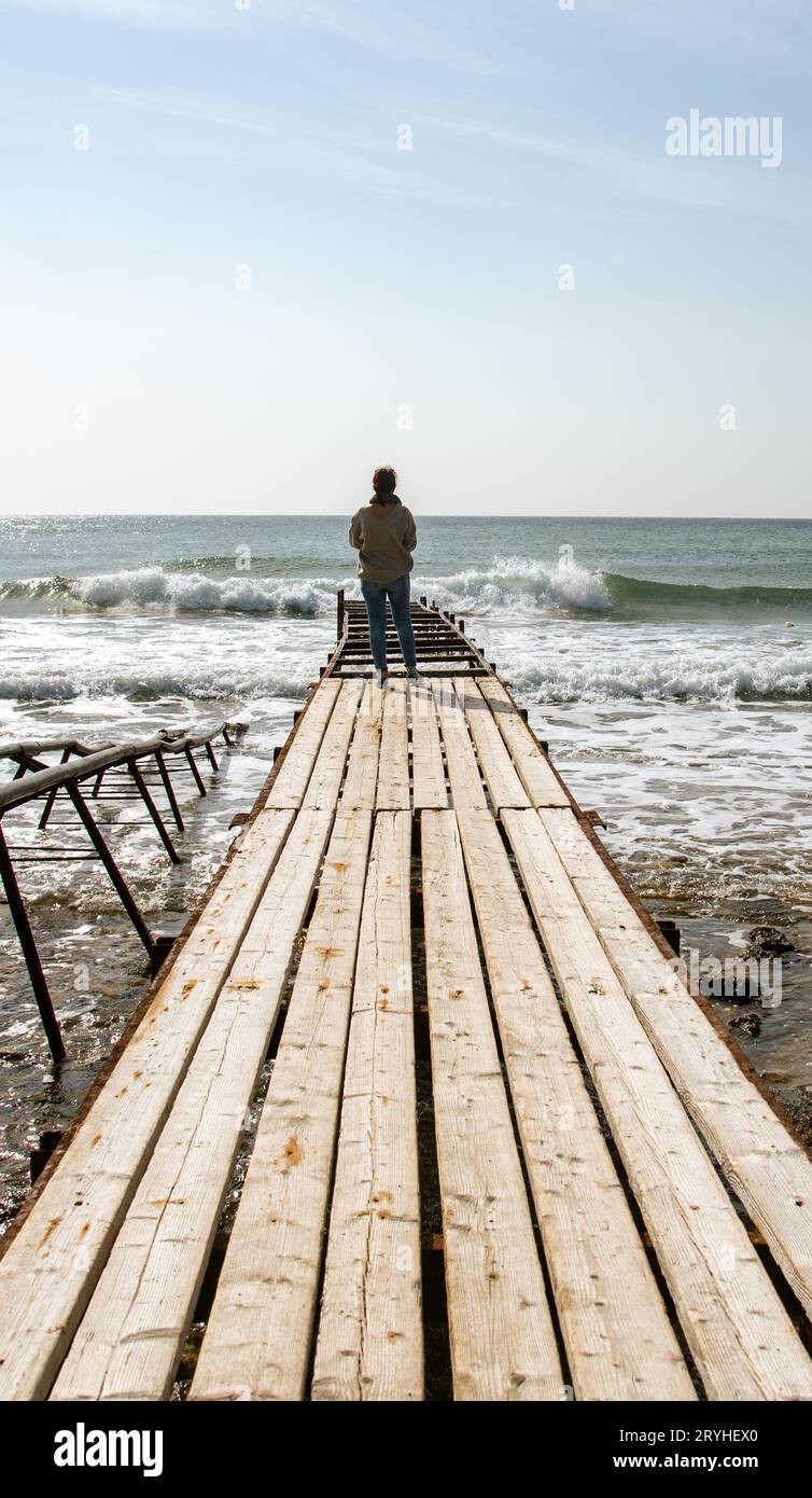 Femme solitaire debout au bord d'un quai en bois dans la mer orageux Banque D'Images