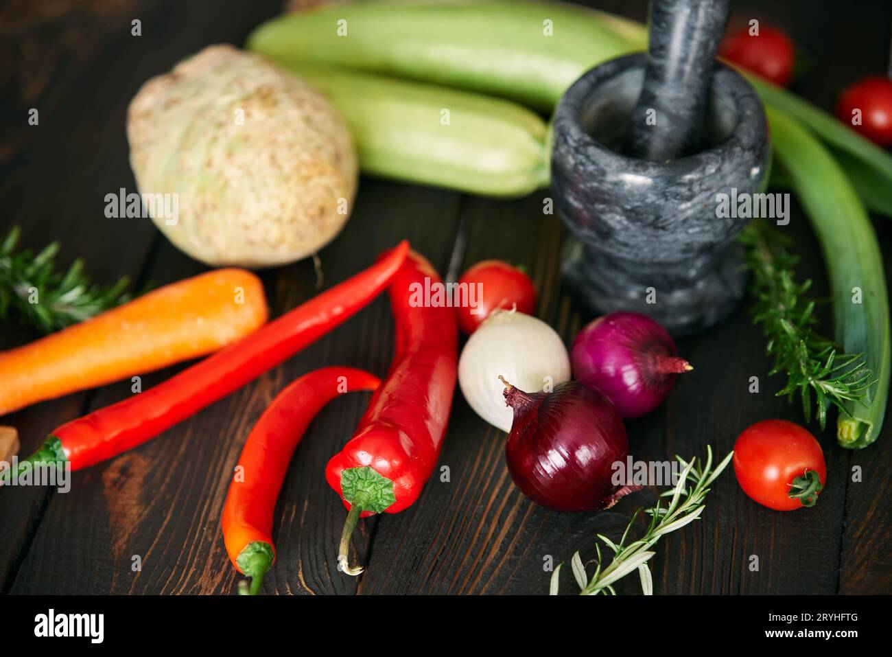 Fond avec des légumes biologiques crus assortis et mortier de marbre noir avec un pilon sur la table de cuisine en bois Banque D'Images