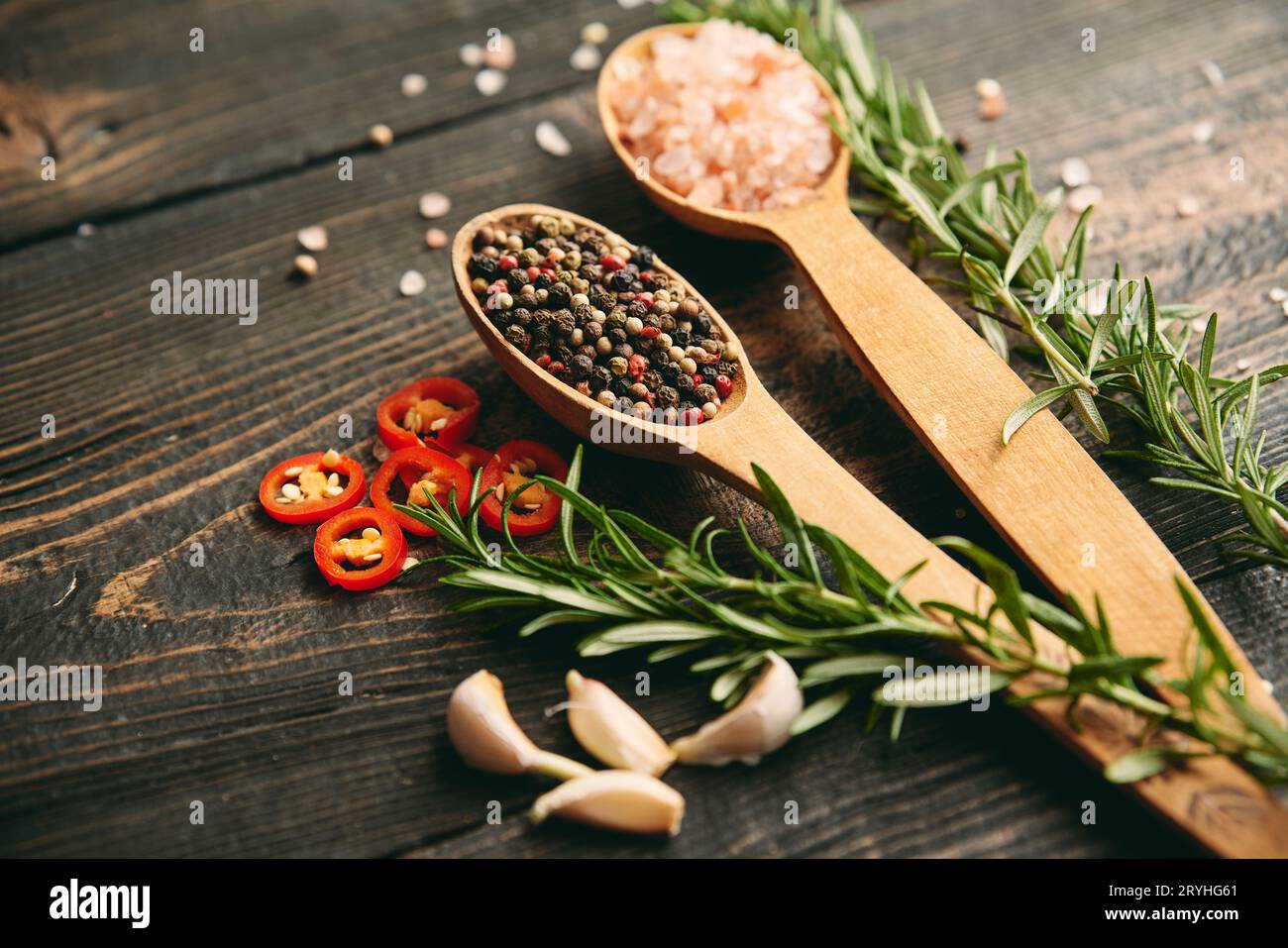 Gros plan photo de grains de poivre mélangés et de sel de mer dans des cuillères en bois, romarin frais et ail sur fond en bois foncé Banque D'Images