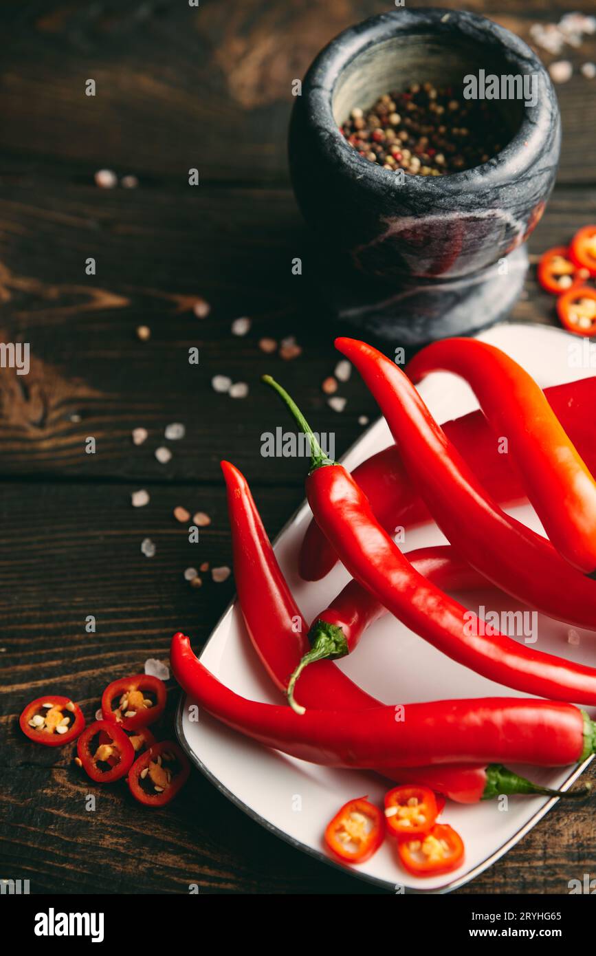 Piments piments rouges et mortier de marbre avec des épices sur la table de cuisine en bois sombre. Banque D'Images