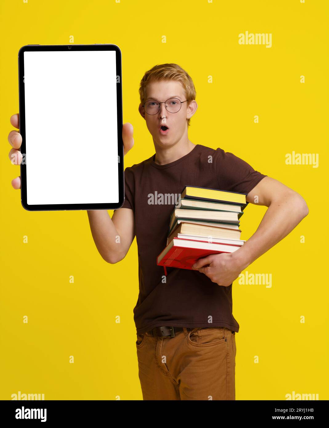 Étudiant surpris tenant des livres et un Tablet PC avec un écran blanc vide pour l'espace de copie sur un fond jaune, mettant en valeur Banque D'Images