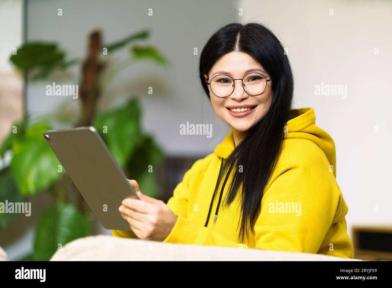 Fille asiatique dans des lunettes, menant avec succès son entreprise de la maison, en utilisant des outils de communication en ligne et des gadgets modernes. Concept Banque D'Images