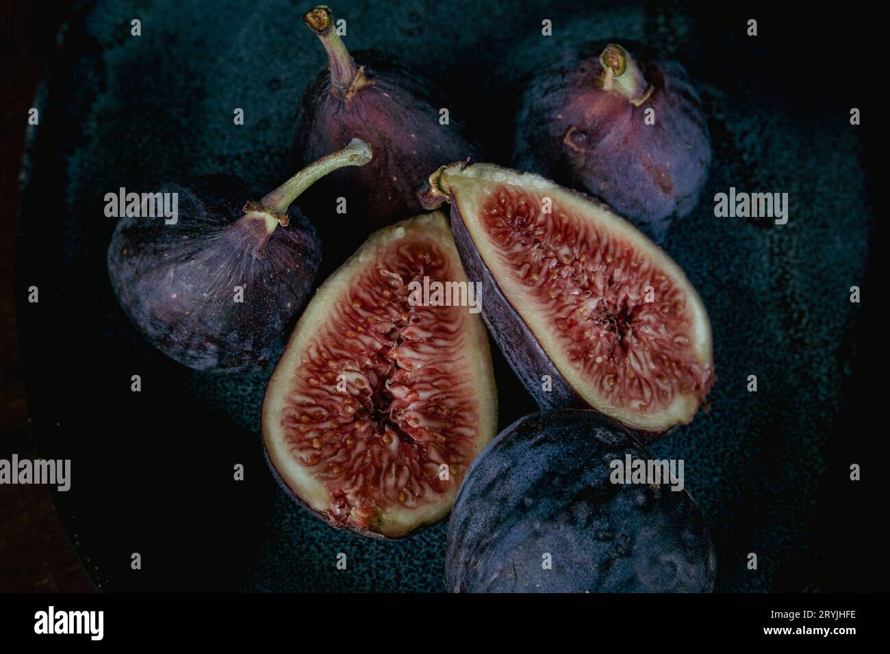 photo rapprochée de figues fruitières ; une figue coupée en 1/2, trois figues entières sur fond sombre. Banque D'Images