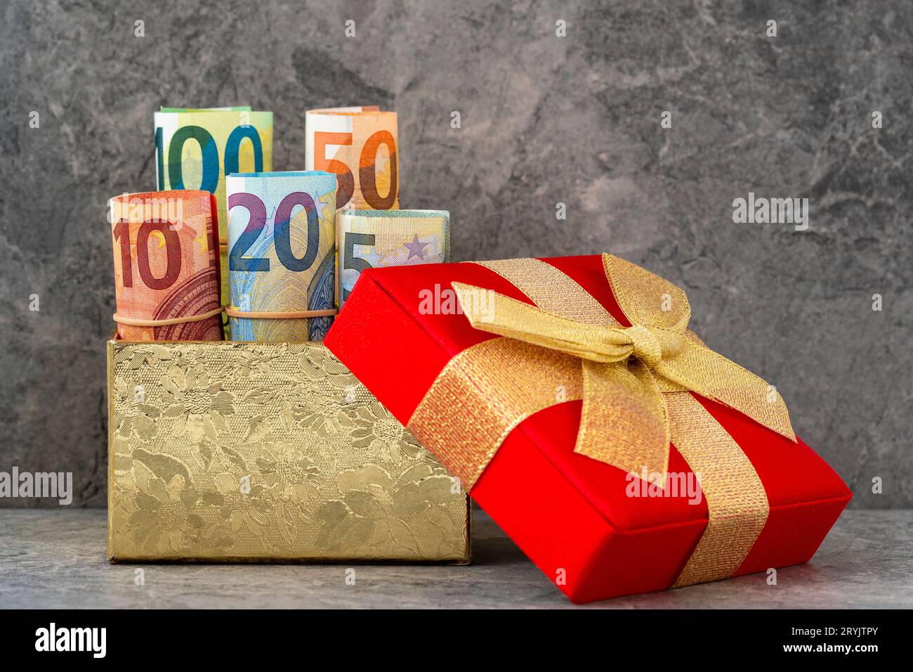 Roulé avec précision des billets en euros dans une boîte cadeau avec un arc doré Banque D'Images