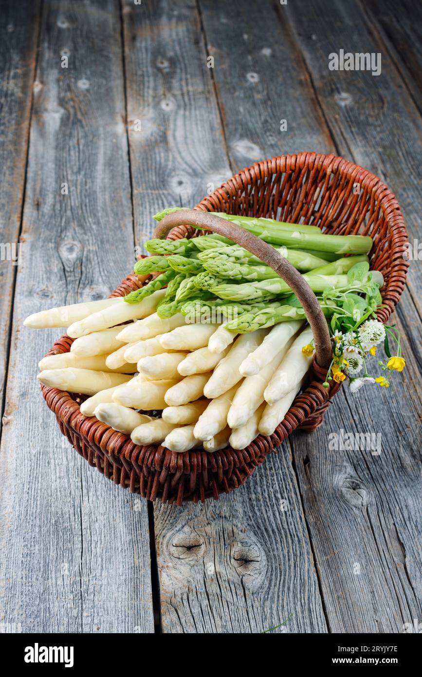 Asperges blanches crues fraîches avec des herbes et des fleurs offertes en gros plan dans un panier sur une planche de bois rustique patiné Banque D'Images