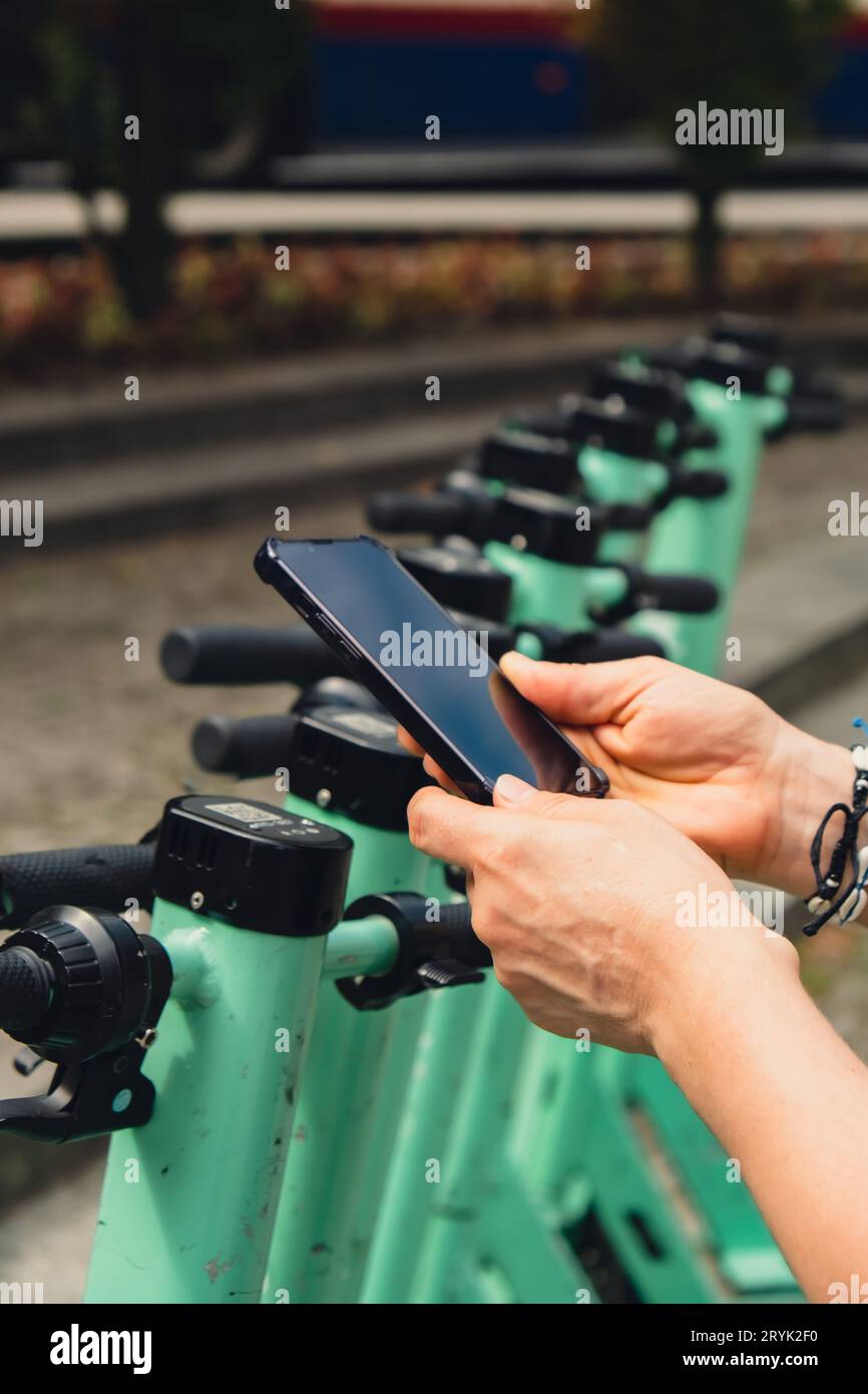Main féminine utilise le téléphone portable pour scanner le code QR sur scooter électrique dans la rue sur e-scooter, application de service de location. tr. Alternative Banque D'Images