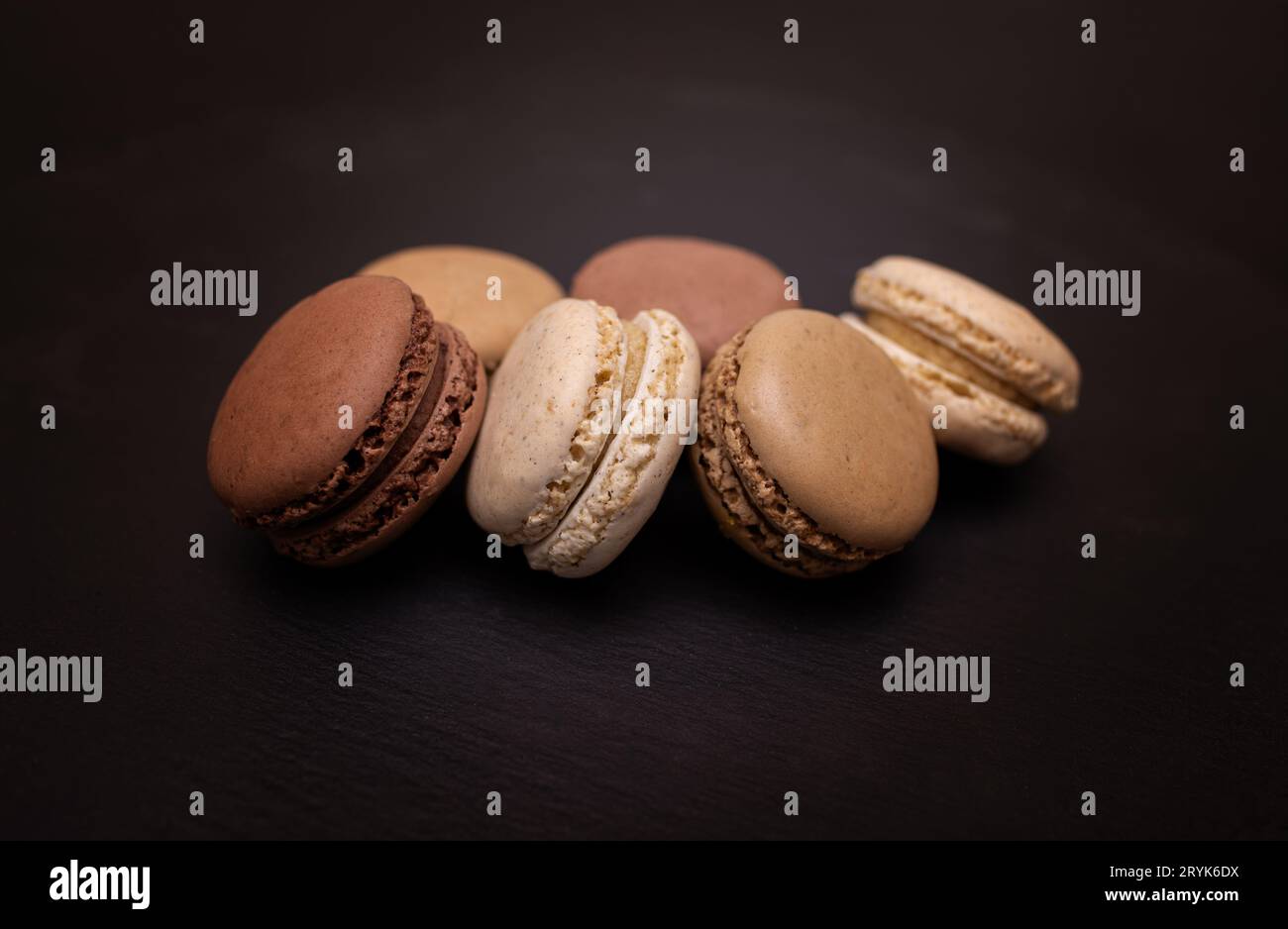 Macarons de couleur beige, marron et crème sur fond ardoise noire. Gros plan dans différentes positions. Mise au point sélective. Banque D'Images