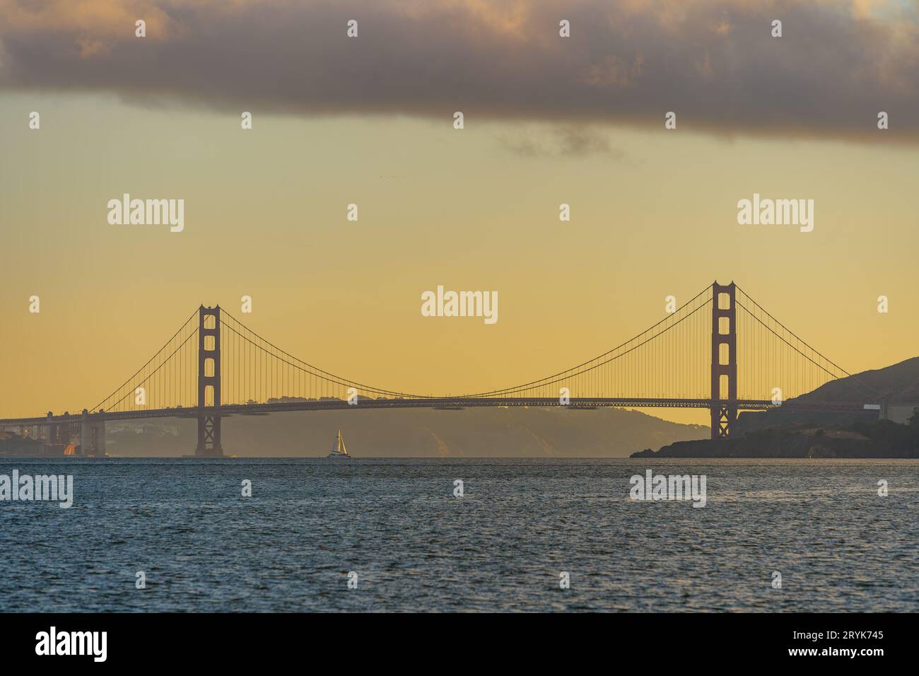 Golden Gate Bridge s'élevant au loin au coucher du soleil avec un voilier en dessous Banque D'Images