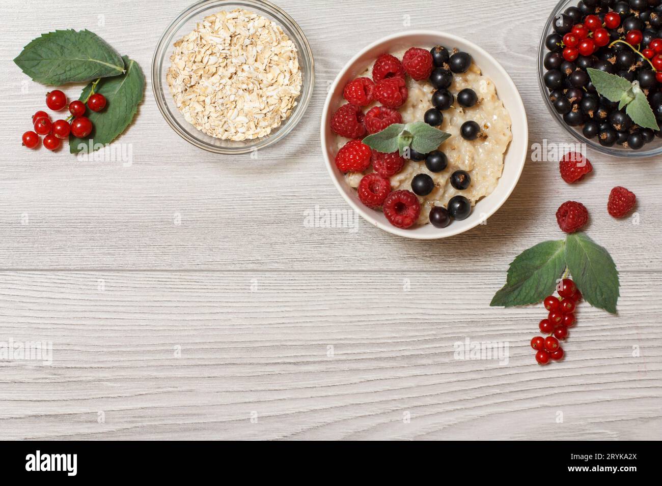 Bouillie d'avoine dans un bol en porcelaine avec baies de groseille et framboises, décorée de feuilles de menthe. Banque D'Images