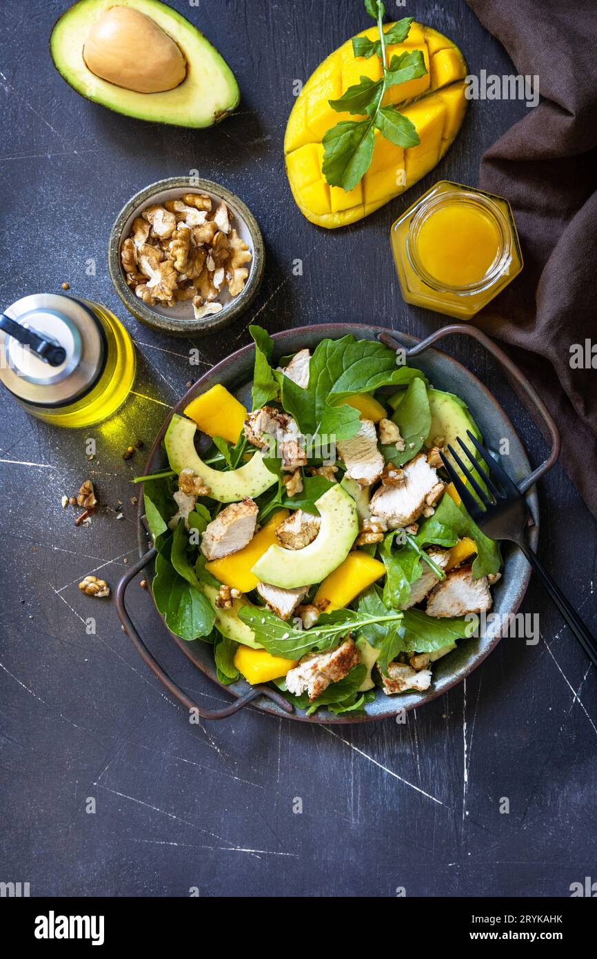Salade diététique saine avec roquette, mangue, avocat, poulet grillé, noix et vinaigrette sur un comptoir en pierre sombre. Haut Banque D'Images