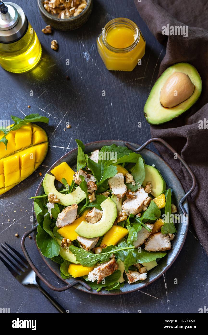 Salade diététique saine avec roquette, mangue, avocat, poulet grillé, noix et vinaigrette sur un comptoir en pierre sombre. COP Banque D'Images