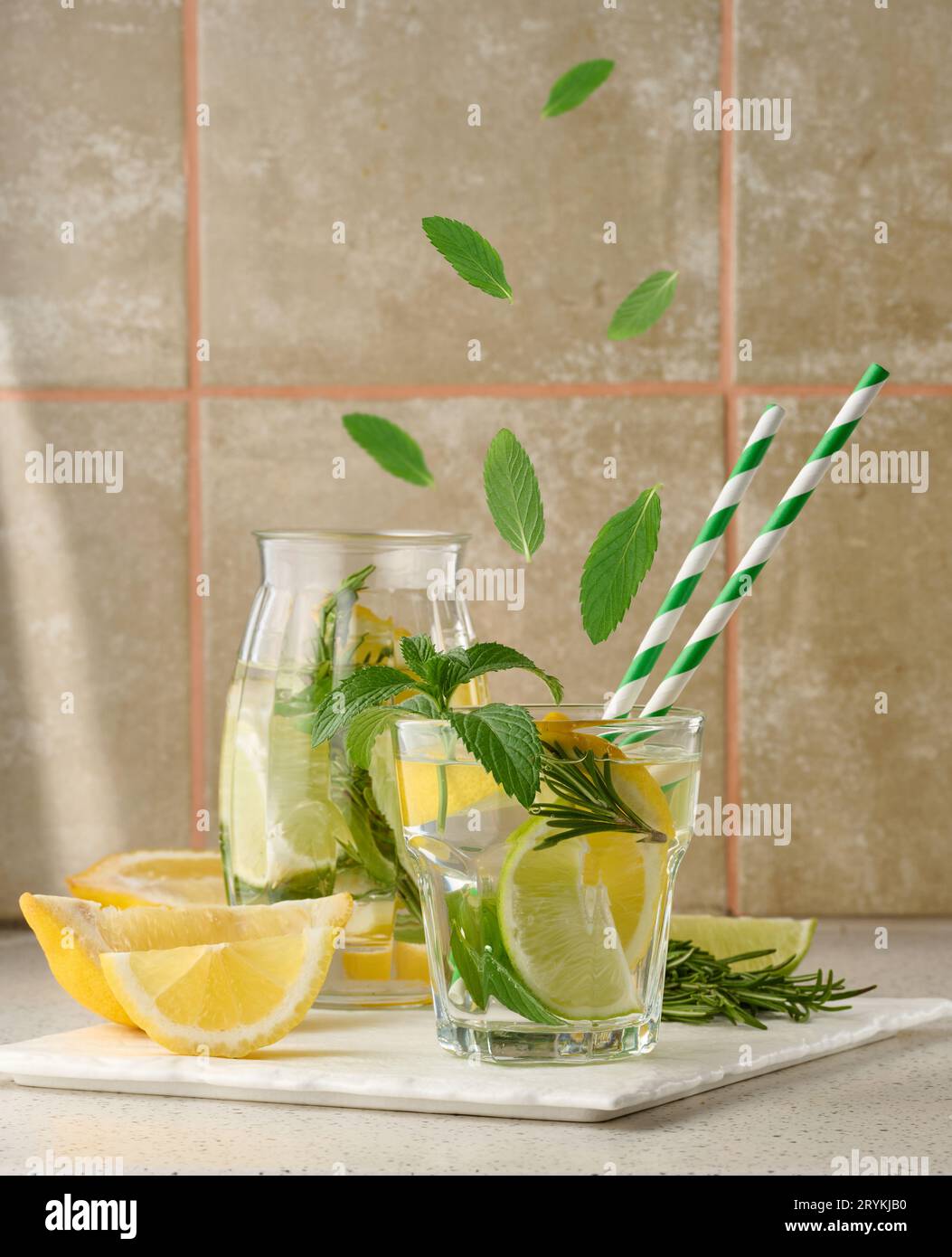 Limonade dans un verre transparent avec citron, lime, brins de romarin et feuilles de menthe sur fond blanc Banque D'Images