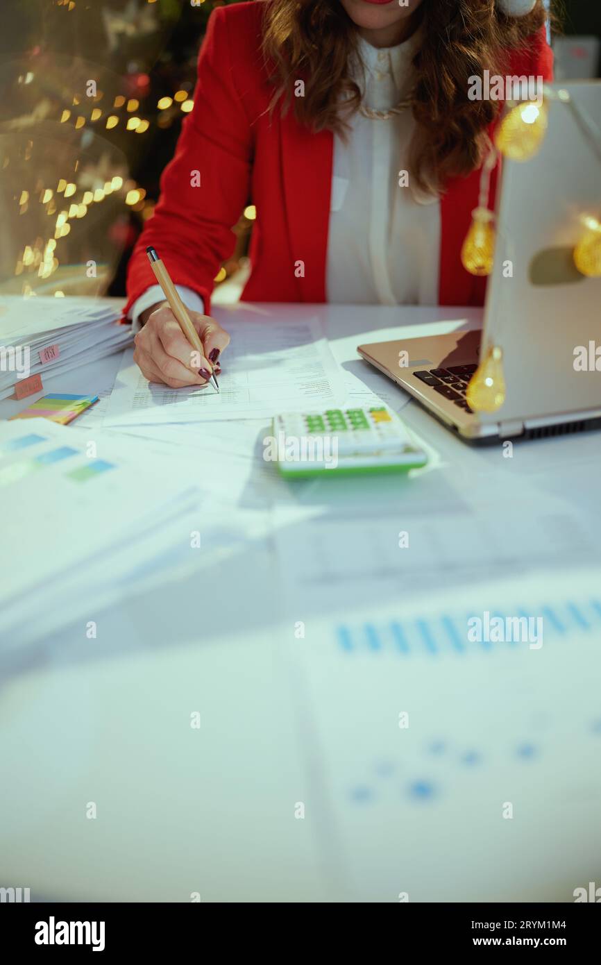 Noël. Gros plan sur femme propriétaire de petite entreprise dans le chapeau de santa et veste rouge avec des documents, ordinateur portable et calculatrice travaillant dans le bureau vert avec C. Banque D'Images