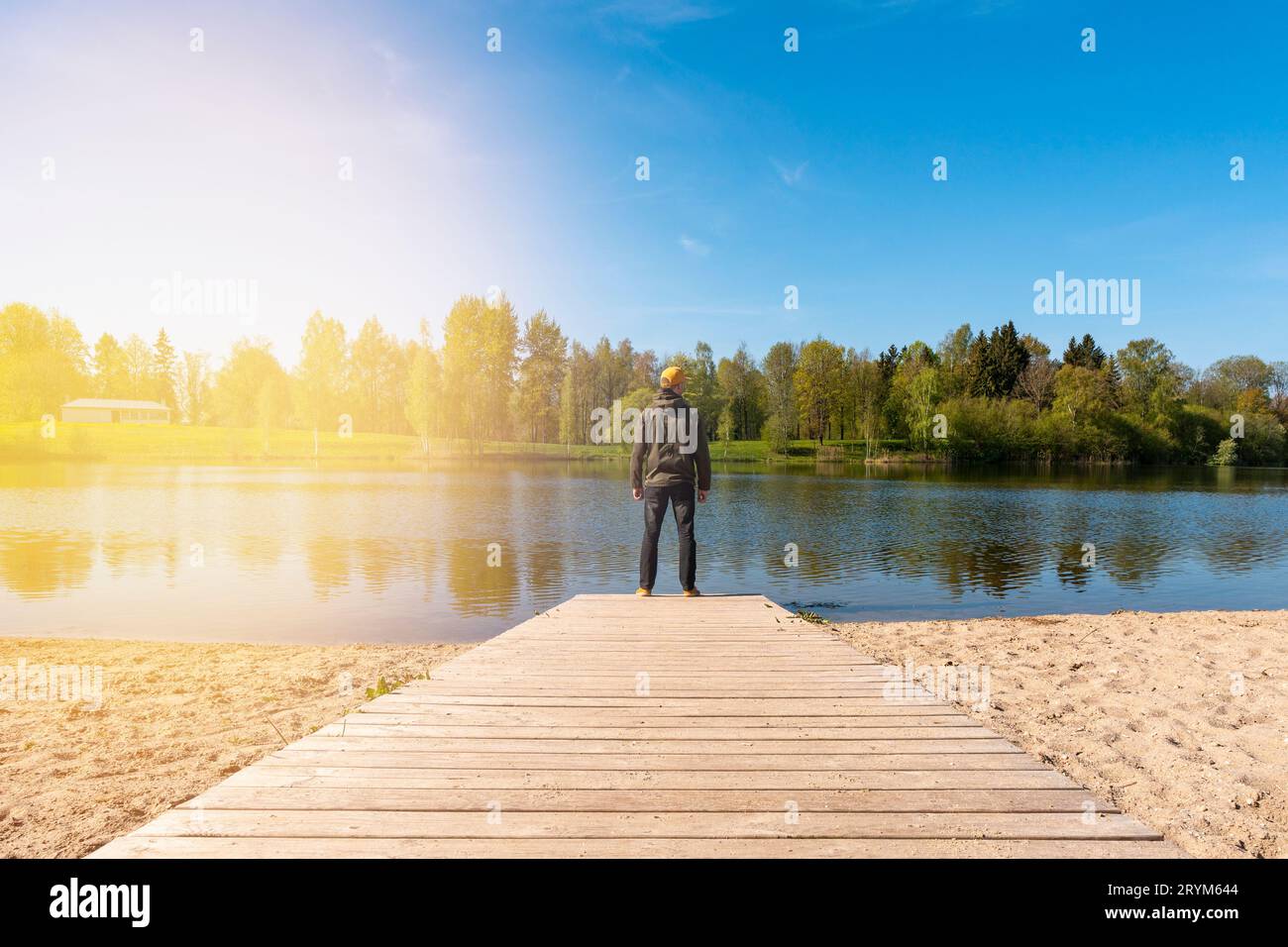 Jeune homme debout seul sur le bord d'une passerelle en bois et regardant le lac Banque D'Images
