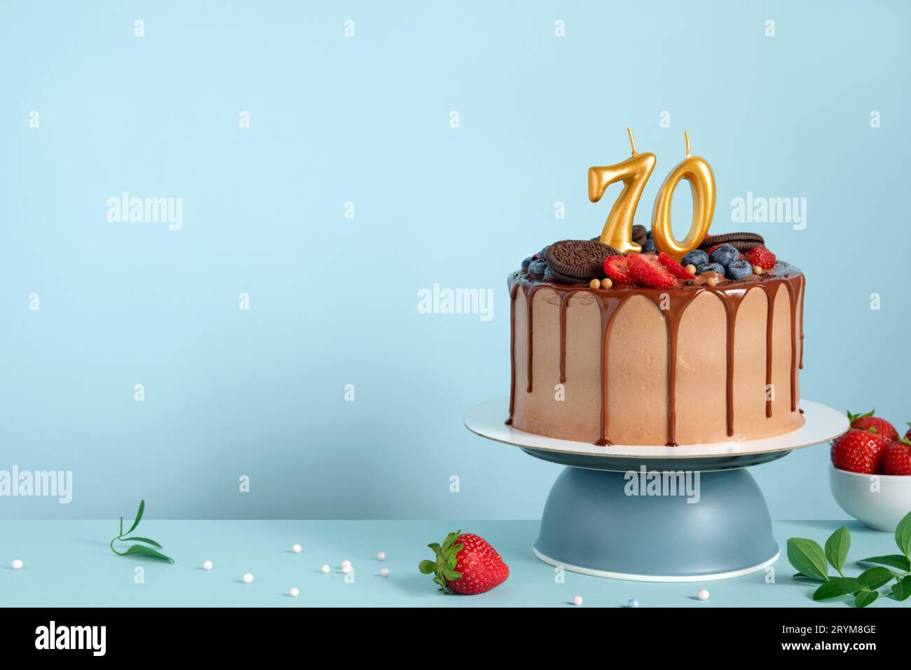 Gâteau d'anniversaire au chocolat avec des baies, des biscuits et le nombre soixante-dix bougies d'or sur fond de mur bleu, espace de copie Banque D'Images