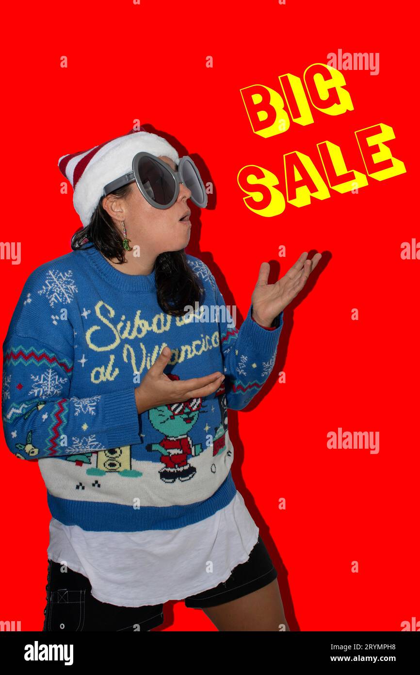 Femme aux cheveux longs, faisant un geste surpris en regardant un grand panneau de vente en lettres jaunes. La femme porte un pull bleu laid, un Christma Banque D'Images