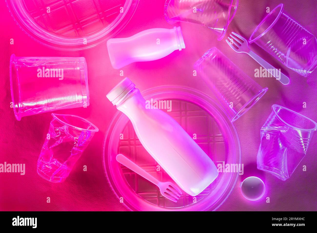 Vaisselle jetable en plastique avec éclairage néon rouge violet. Concept de problème écologique Banque D'Images