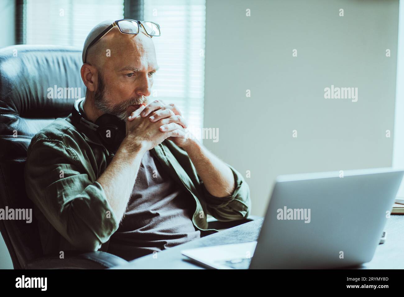 Homme d'âge moyen entièrement concentré sur le travail, il regarde attentivement l'ordinateur sur la table. Profondément dans la pensée, il réfléchit sur la tâche ou le problème à Banque D'Images