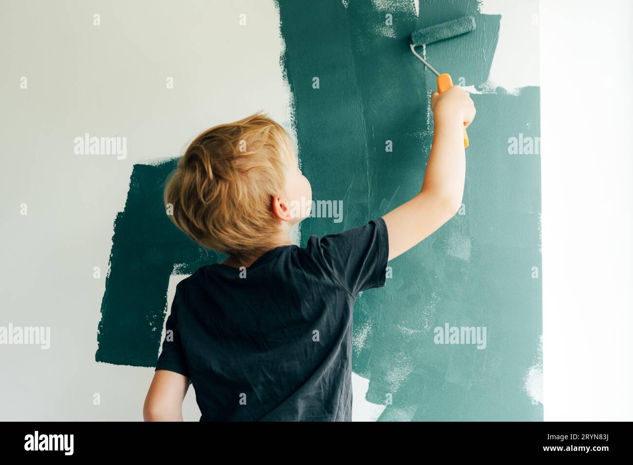 Un garçon peint un mur dans une pièce près de la fenêtre.Mises à jour dans l'appartement.Réparez-vous. Banque D'Images