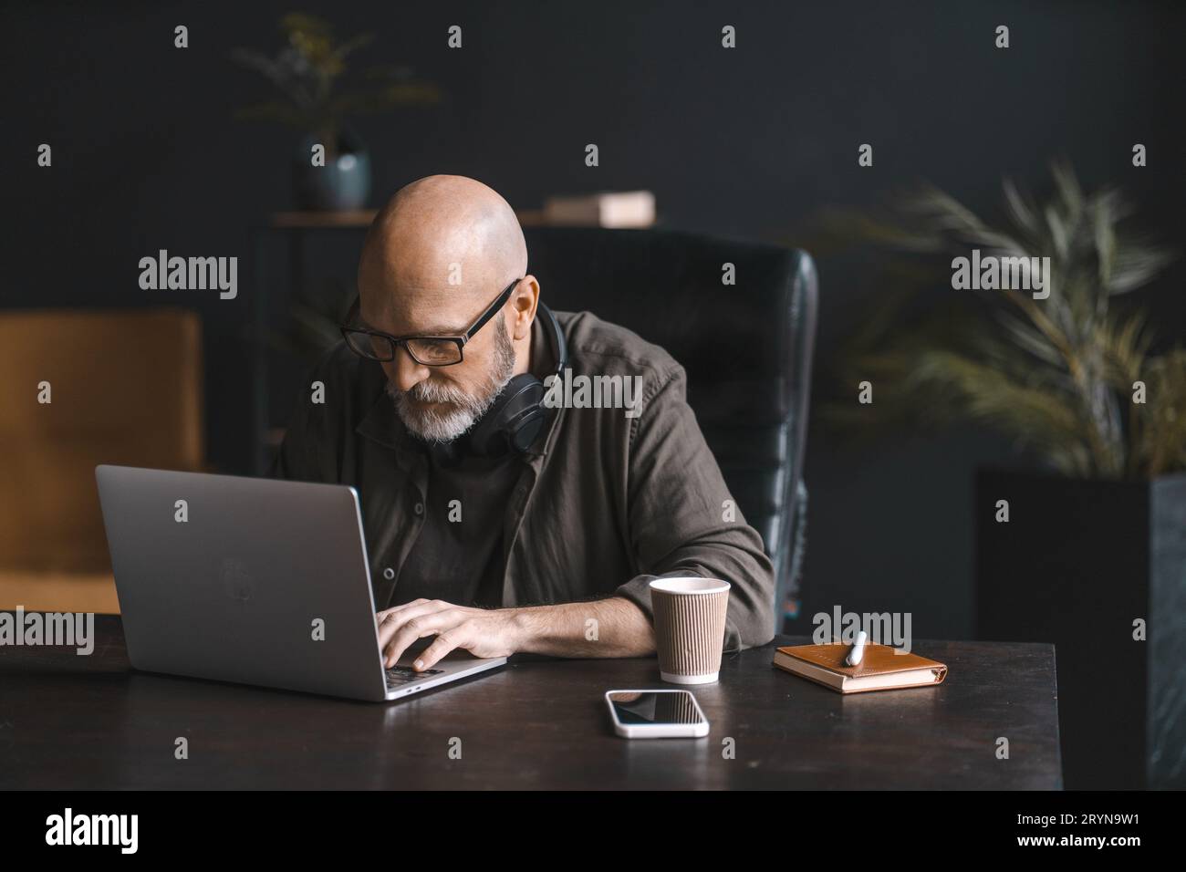 Concept de travailleur acharné, un homme d'âge mûr dévoué passe la journée immergé dans le travail, utilisant assidûment l'ordinateur portable avec concentration et détermination Banque D'Images