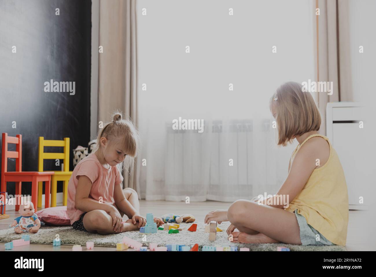 Enfants jouant avec des blocs de construction de jouets en bois colorés, briques. Enfants assis sur le sol à la chambre à coucher blanche ensoleillée ou à la maternelle, salle de jeux de garderie Banque D'Images