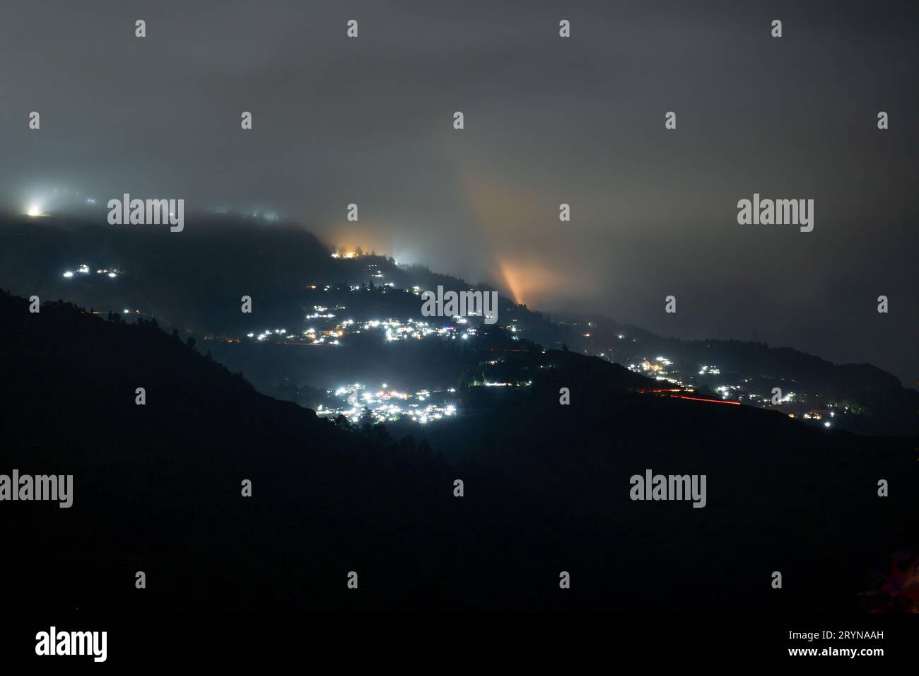 Photo de nuit montrant le village de darjeeling niché au milieu des montagnes de l'himalaya avec des lumières orange et bleues Banque D'Images