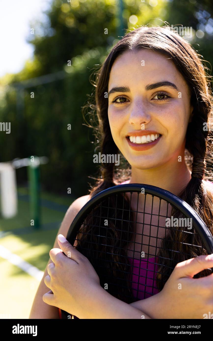 Gros plan d'une jeune femme biraciale souriante avec raquette de tennis sur un court de tennis par beau soleil Banque D'Images