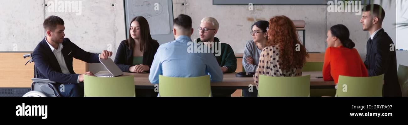 Photo large recadrée d'un groupe diversifié de professionnels d'affaires, y compris une personne handicapée, réunis dans un bureau moderne Banque D'Images