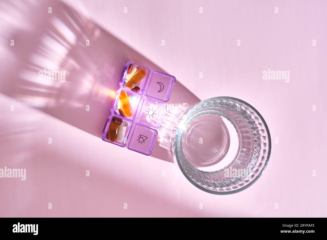Boîte à pilules lumineuse avec différentes pilules et vitamines à côté d'un verre d'eau. Banque D'Images