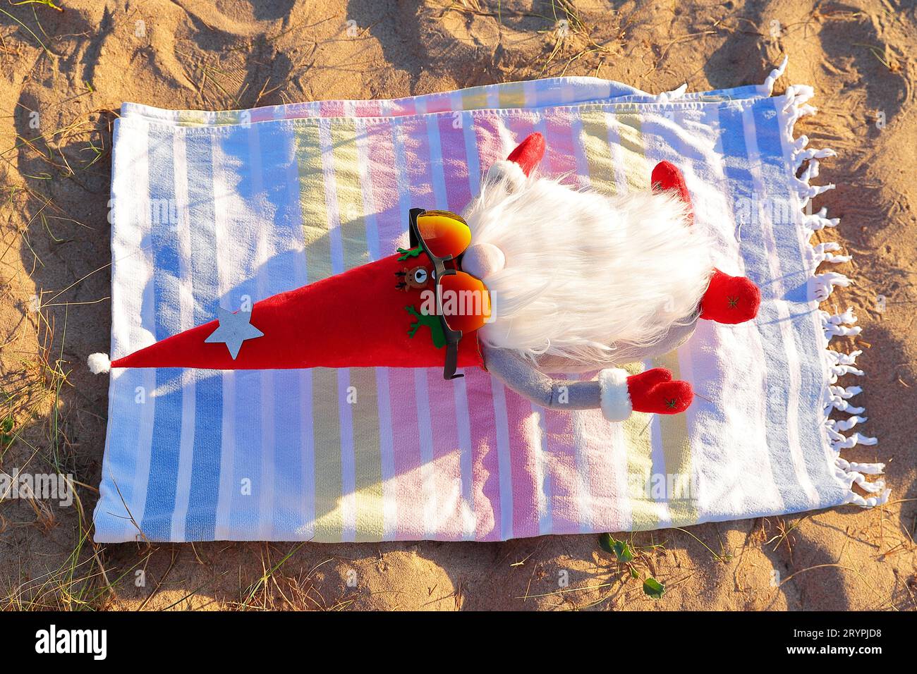 Gnome de Noël bains de soleil se relaxant sur sa serviette sur la plage. Concept relaxation et qualité de vie. Horizontal Banque D'Images