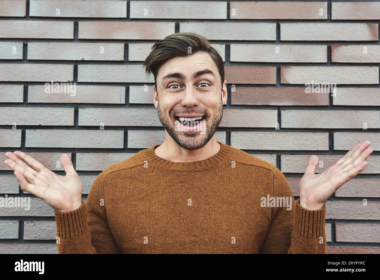 Gros plan Happy Handsome Man dans la mode tendance penché sur Old Brick Wall tout en regardant la caméra. Banque D'Images