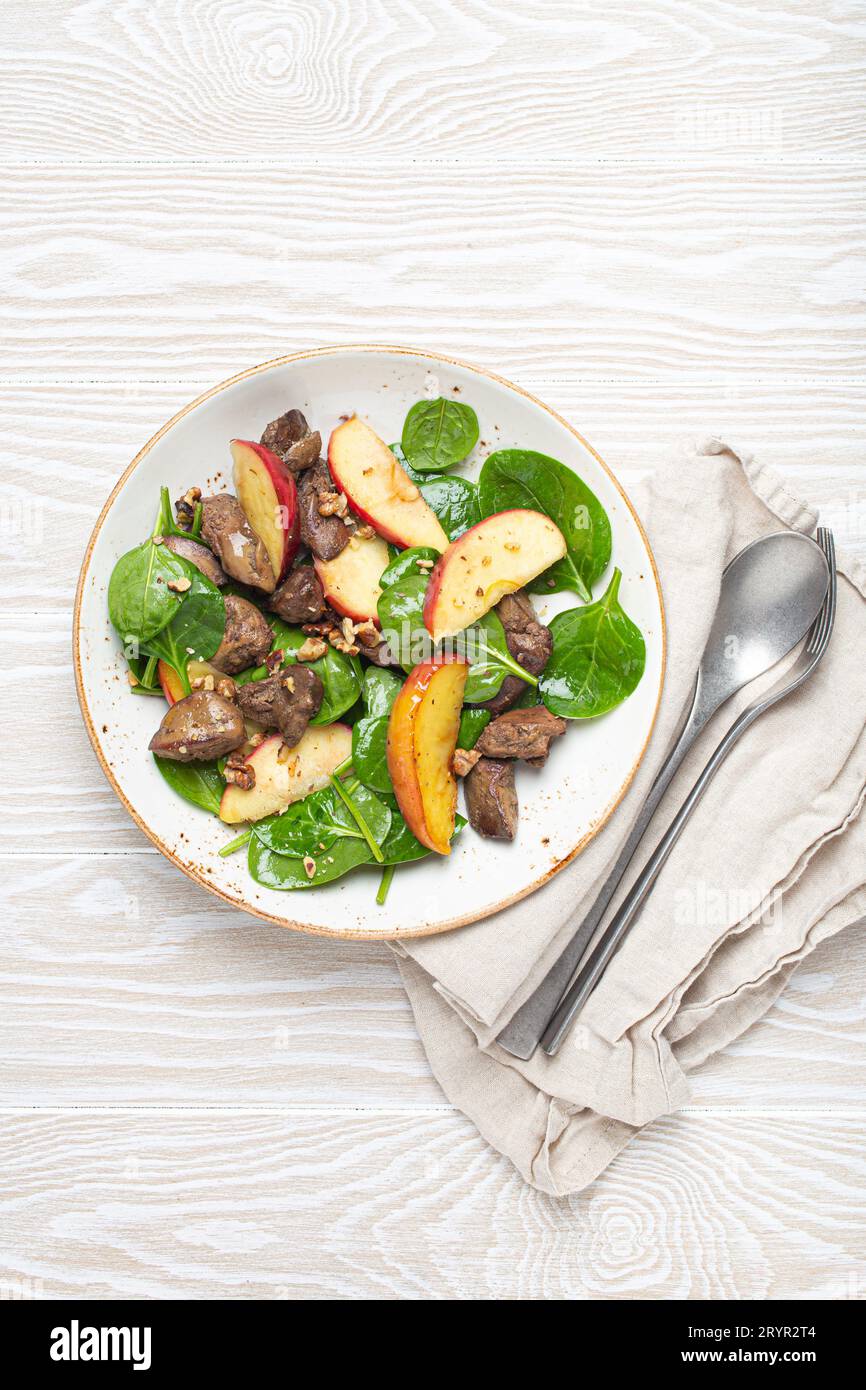 Salade saine avec des ingrédients riches en fer foie de poulet, pommes, épinards frais et noix sur plaque en céramique blanche, bois blanc B Banque D'Images