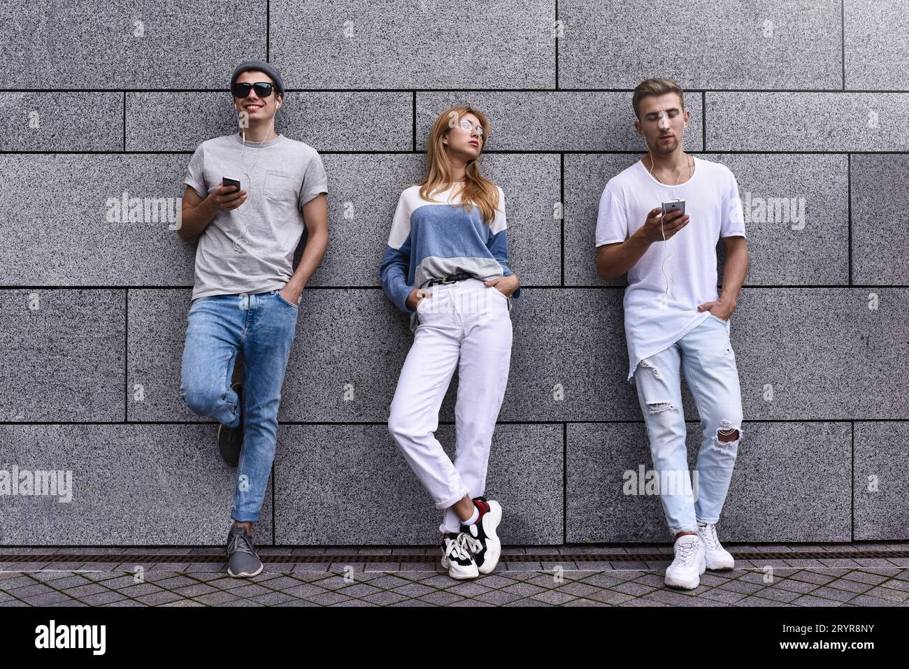 Portrait de mode de trois meilleurs amis posant dans la rue, portant une tenue élégante et un Jean contre le mur gris . Banque D'Images