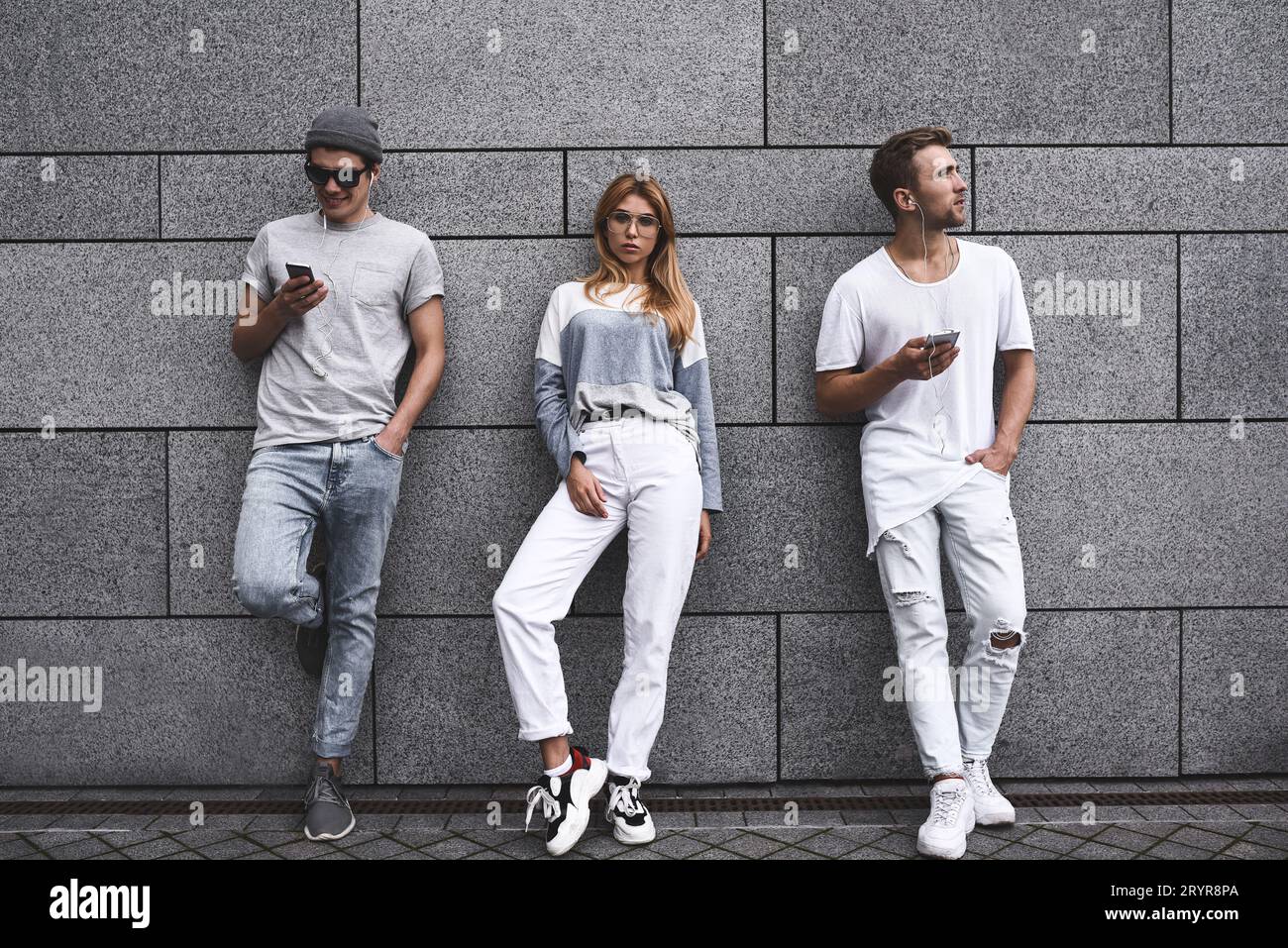 Portrait de mode de trois meilleurs amis posant dans la rue, portant une tenue élégante et un Jean contre le mur gris . Banque D'Images