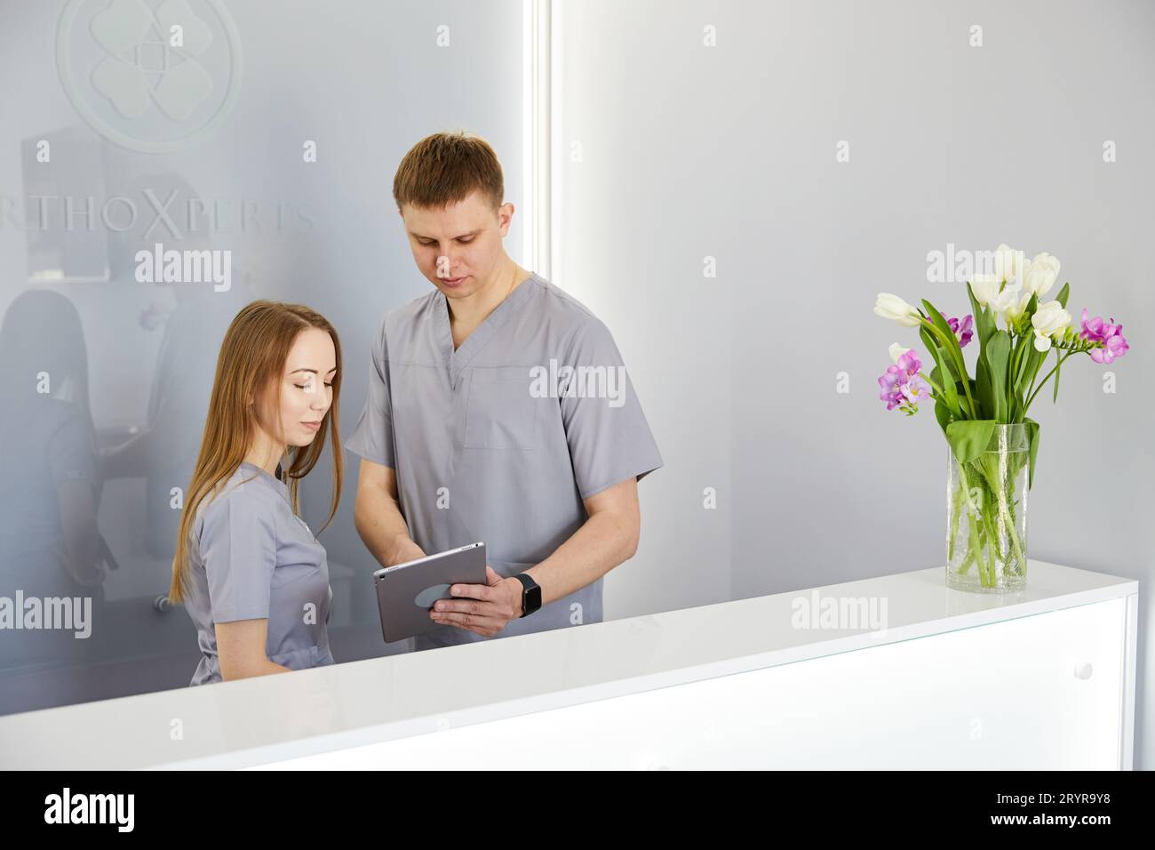 Dentiste avec infirmière dentaire dans un cabinet dentaire moderne utilisant un PC tablette portant l'uniforme. Spécialiste en orthodontie et assisant à la réception en clinique dentaire d Banque D'Images