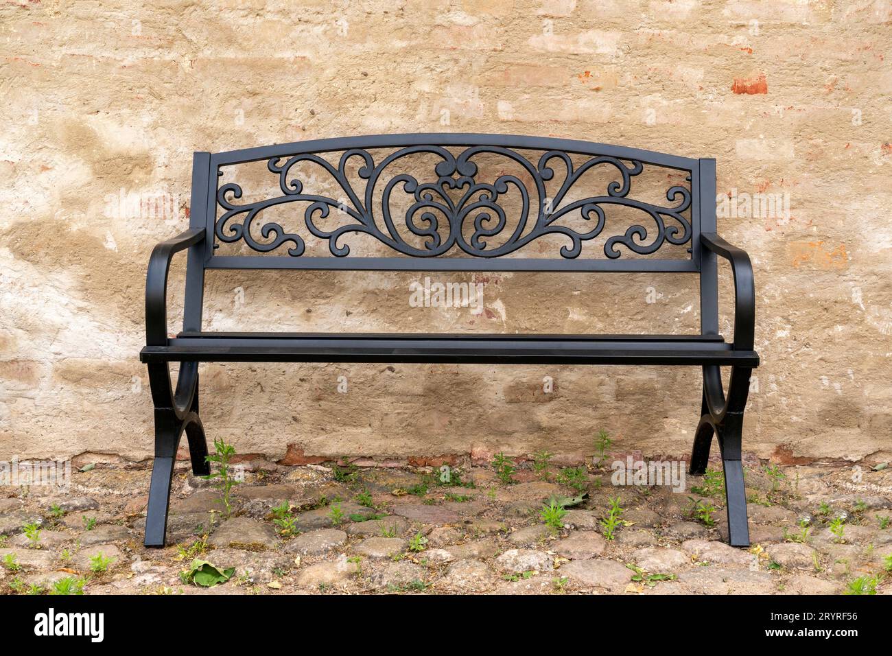 Un banc en métal vide contre un vieux mur Banque D'Images