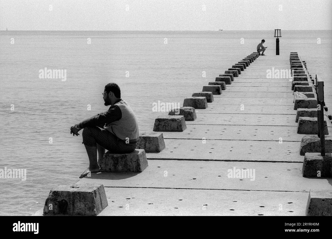 Deux personnages assis sur une jetée de plage à Bournmouth UK apparemment absents de tout autre tgouriste ou nageur dans cette image en noir et blanc prise en août 1989. Jetée de plage Bournmouth 19890808 Banque D'Images