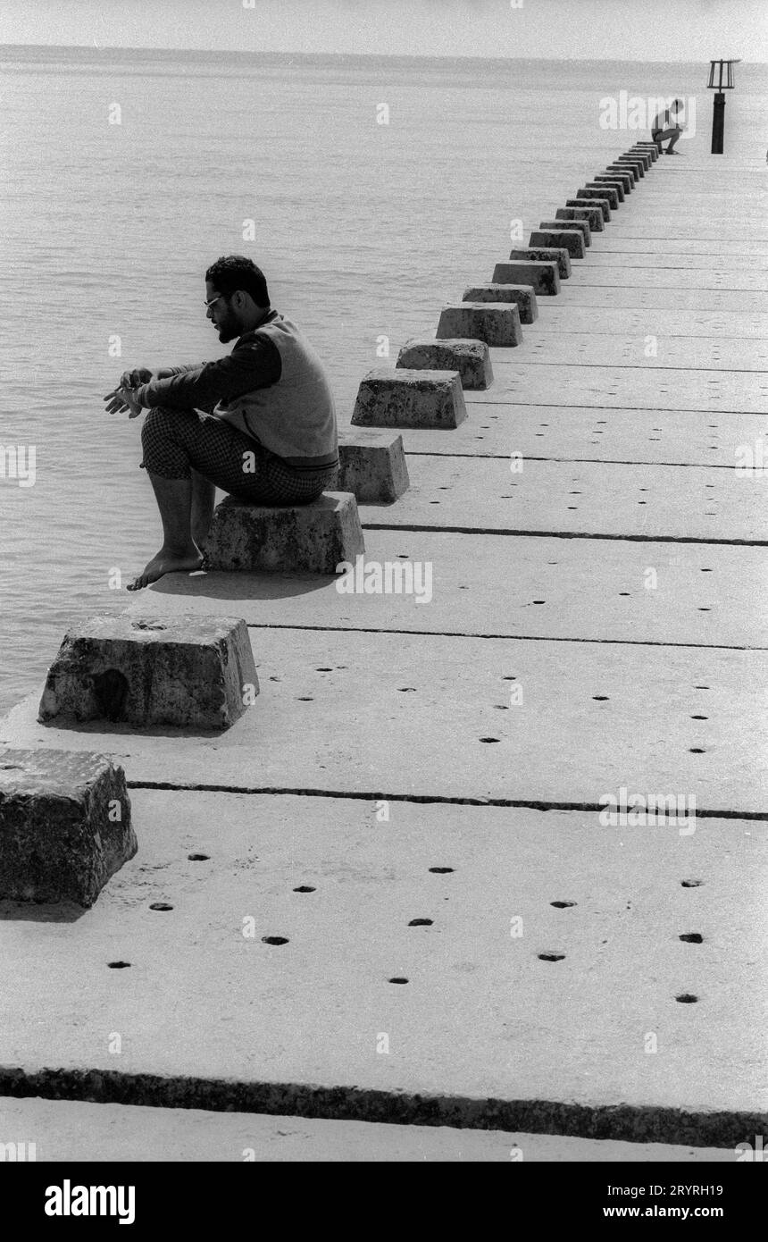 Deux personnages assis sur une jetée de plage à Bournmouth UK apparemment absents de tout autre tgouriste ou nageur dans cette image en noir et blanc prise en août 1989. Jetée de plage Bournmouth 19890808 Banque D'Images