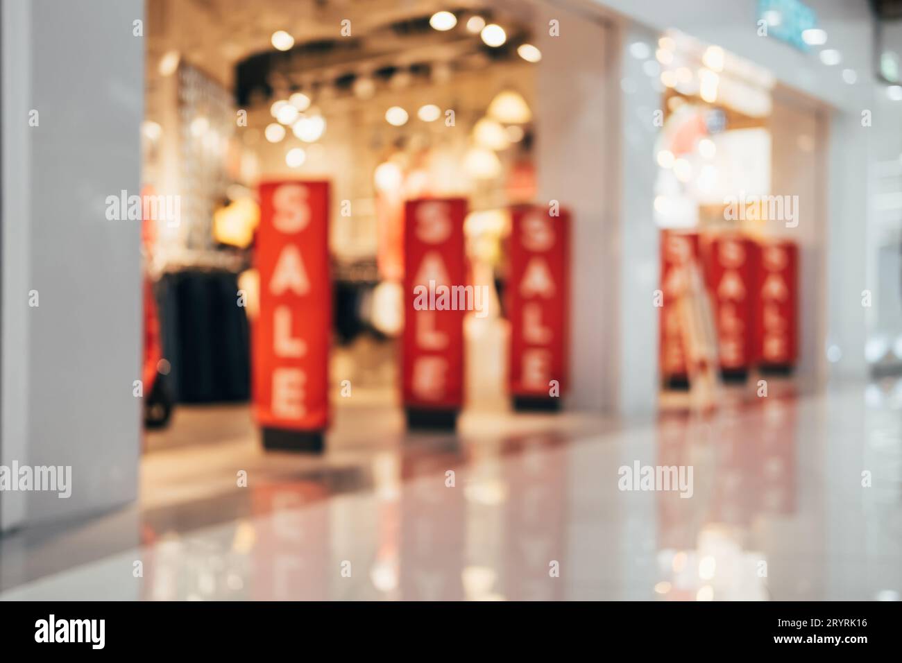 Bannières rouges avec texte DE VENTE au magasin de vêtements. Fond flou abstrait de l'intérieur du centre commercial Banque D'Images