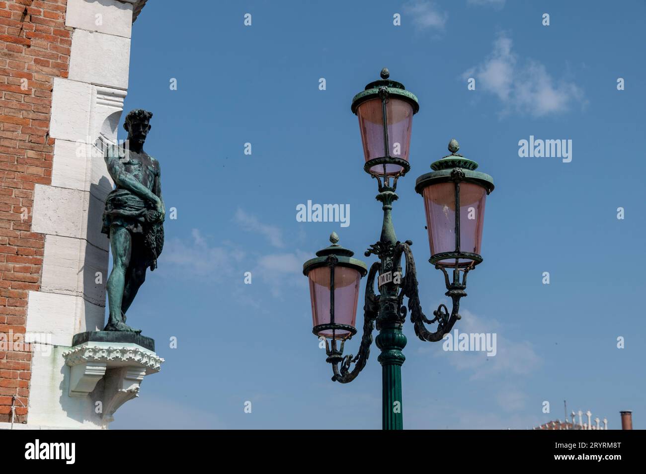 Une petite statue murale à côté de l'un des lampadaires ornementaux familiers de Venise dans la région de la Vénétie au nord de l'Italie. Banque D'Images