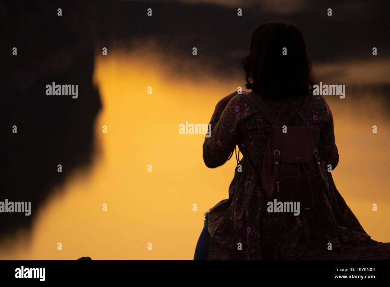 Une vue de l'arrière d'une fille de touriste se trouve sur une montagne et admire la belle vue et l'aube ou le coucher du soleil ou le lever du soleil. Femme assise sur un rocher au-dessus de M. Banque D'Images