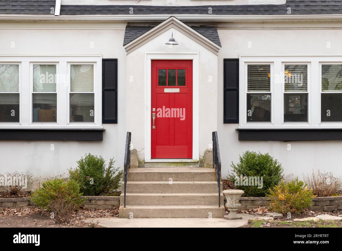 Un détail de porte d'entrée rouge sur une maison blanche avec des marches en béton et des rampes en fer menant à la porte. Banque D'Images