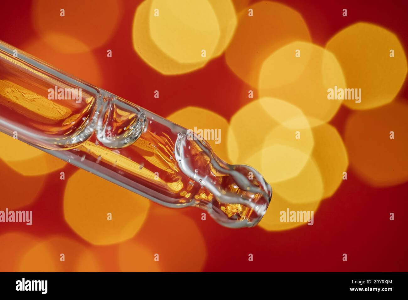 Pipeter avec du sérum sur un fond rouge de vacances avec du bokeh. Banque D'Images