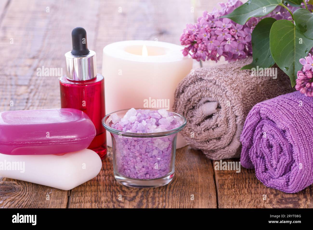 Bouteille rouge avec de l'huile aromatique, les bougies, savon, bol avec du sel de mer, de fleurs lilas et des serviettes pour salle de bains procédures sur les planches de bois. Produit Spa Banque D'Images