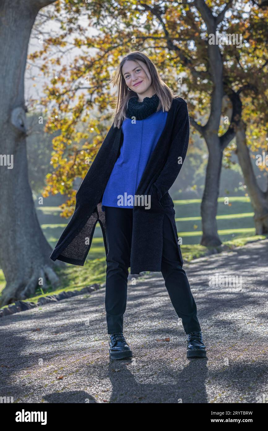 Une femme habillée en tenue d'automne confortable se dresse au milieu du feuillage vibrant de grands arbres ornés de feuilles d'automne Banque D'Images