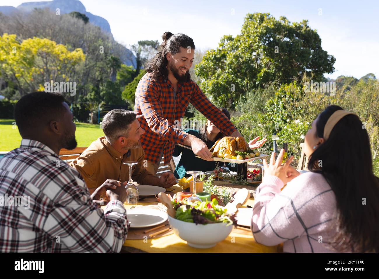 Heureux et divers amis masculins et féminins servant le repas de célébration de Thanksgiving dans le jardin ensoleillé Banque D'Images